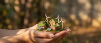 Close-up of a hand holding a small green plant with wind turbines, symbolizing renewable energy and sustainable development for environmental conservation concepts.