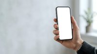 Hand holding smartphone with blank white screen in modern office environment, suitable for app mockups and digital marketing campaigns.