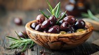 Fresh black olives in rustic olive wood bowl with rosemary sprigs on dark wooden table, Mediterranean cuisine ingredients for gourmet cooking.