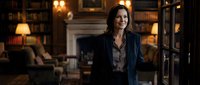 Professional businesswoman in elegant suit standing confidently in luxurious library office with warm lighting and classic decor for corporate success concepts.