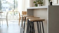 Modern kitchen bar stools with wooden seats and black metal legs positioned at white counter in bright, minimalist dining space with natural light.