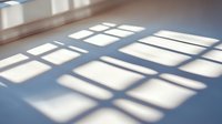 Geometric window light shadows cast on blue floor creating abstract pattern of rectangles and squares in minimalist interior space.
