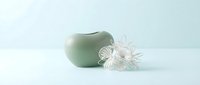 Jade green ceramic vase with translucent glass flower sculpture on white surface, minimalist home decor and interior design styling.
