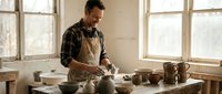 Male potter crafting ceramic bowls on wheel in bright studio workshop. Artisan hands shaping clay pottery with natural window light and rustic wooden workspace.