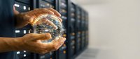 Hands holding glowing globe with digital network connections in server room environment, representing global technology, data connectivity, and cloud computing infrastructure.