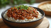 Hearty lentil curry served over steamed white rice in rustic ceramic bowl, garnished with fresh chopped herbs, photographed with selective focus on wooden surface.