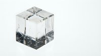 Clear ice cube with black particles and water droplets frozen inside, isolated on white background for beverage, cocktail, and cooling design projects.