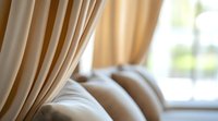 Soft beige curtains and plush white pillows create serene bedroom atmosphere with natural window light and gentle morning glow, expressing comfort and tranquility.