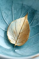 Golden dried leaf on turquoise ceramic bowl with textured surface creates elegant natural contrast for spa, wellness and mindfulness concepts.