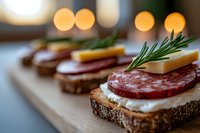 Gourmet open-faced sandwiches with cured meat, cheese and fresh rosemary garnish arranged on whole grain bread slices, perfect for catering, restaurant menus and food styling.