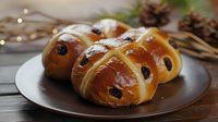 Freshly baked hot cross buns with raisins on plate, festive holiday pastry with glossy golden crust and traditional cross pattern.