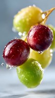 Fresh red and green grapes with water drops in macro photography against light gray background, showing natural freshness and juicy texture.