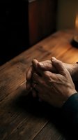 Elderly hands clasped in prayer on wooden table with warm lighting creating peaceful spiritual atmosphere for meditation and faith concepts.