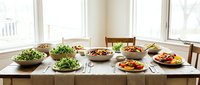 Rustic wooden dining table set with an abundant spread of fresh salads and colorful vegetable dishes in a bright, sunlit room.