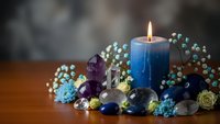 Blue candle burning surrounded by healing crystals, gemstones and dried flowers on wooden surface. Spiritual wellness meditation aromatherapy relaxation concept.