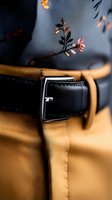 Elegant black leather belt with silver buckle detail against mustard yellow fabric, with delicate floral pattern in soft focus background creating luxury mood.