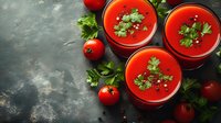 Fresh tomato gazpacho soup garnished with parsley served in glass bowls on dark rustic background with raw vegetables and herbs, top view.