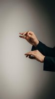 Hands in a black suit gesturing expressively against a neutral gray background, conveying control, direction, or magic performance.