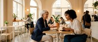Two diverse businesswomen having coffee meeting in modern bright cafe discussing work collaboration and partnership opportunities.