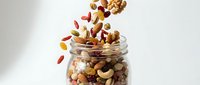 Mixed nuts and dried fruits pouring from glass jar. Healthy snack mix with almonds, cashews, raisins, and berries for nutrition and wellness.