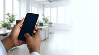 Male hand holding smartphone with blank screen in modern office environment with natural light and plants.