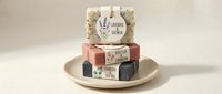 Stacked artisan soap bars with lavender and natural ingredients on ceramic plate, isolated on white background for cosmetic retail and wellness product design.