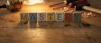 Wooden blocks spelling MASTERY on a rustic workbench with tools and wood shavings, warm light highlighting craftsmanship and skill concept.