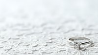 Elegant diamond engagement ring on delicate white lace fabric background for wedding and romance themes.