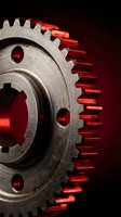Metal gear wheel with red lighting effect on dark background for industrial and mechanical engineering concepts.