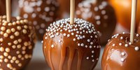 Caramel candy apples decorated with white sugar pearls on wooden sticks. Close up view showing glossy coating and dripping caramel. Sweet autumn treat.