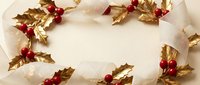 Golden holly leaves with red berries arranged in decorative border on white wooden background for Christmas holiday designs and seasonal greeting cards.