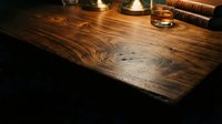 Rustic wooden desk with dark grain texture, vintage books, and whiskey glass on black background, suitable for office and library design projects.