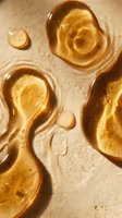 Golden honey or amber gel drops with organic shapes on beige textured surface, suitable for skincare, cosmetics, wellness and beauty product packaging design.