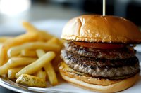 Juicy double beef burger with melted cheese on golden brioche bun served with crispy french fries on white plate, close-up shot with selective focus.
