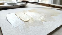 Fresh pasta dough being prepared on floured surface in professional kitchen with rolling pin and cooking utensils in background for culinary projects.