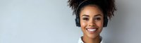 Young African American woman with curly hair wearing headset smiling at camera against gray background for customer service and call center concepts.