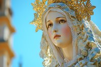 Religious statue adorned with ornate golden crown and white lace veil against blue sky background, depicting serene expression and delicate craftsmanship.