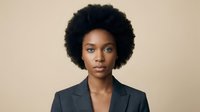 Professional African American businesswoman with natural afro hairstyle wearing dark blazer against neutral beige background for corporate presentations.