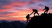Team of climbers helping each other reach mountain summit at dramatic sunset with pink and purple sky. Teamwork and leadership concept for business success.