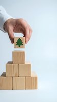 Hand placing wooden block with green tree symbol on pyramid of natural wood cubes representing environmental sustainability and eco-friendly business growth.