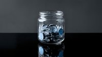 Glass jar filled with silver coins on dark reflective surface for savings and financial planning concepts.