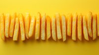 French fries arranged in straight line on bright yellow background. Golden crispy potato strips create minimalist food composition with strong visual contrast.