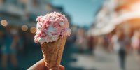 Strawberry ice cream cone with sprinkles held in hand on blurred city street background. Summer dessert treat for food blogs and restaurant menus.