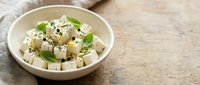 Fresh tofu cubes with herbs and black sesame seeds in ceramic bowl on rustic wooden table background for healthy vegetarian cooking and meal preparation.
