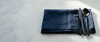 Dark blue linen napkin with fork, knife and spoon on white marble surface for dining and table setting design projects.