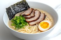 Traditional ramen bowl with sliced chashu pork, soft boiled egg, green onions, nori seaweed in creamy tonkotsu broth and fresh noodles on white background.