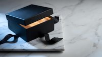 Elegant black gift box with golden interior and silk ribbon on marble surface for luxury packaging and premium product presentation.