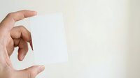 Male hand holding blank white card or paper against neutral background for business, marketing, or promotional use.