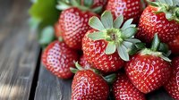 Fresh ripe strawberries with green leaves scattered on dark wooden background, macro shot with selective focus showing juicy red fruit texture.