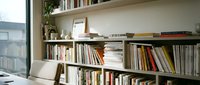 Modern home library with wooden bookshelves filled with books and magazines. Cozy reading corner with natural light from window. Contemporary interior design.